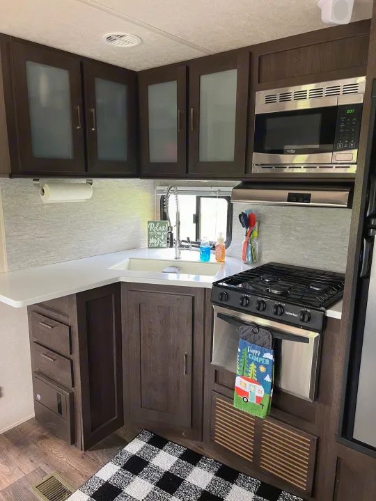 Modern RV rental kitchen with dark wood cabinets, white countertops, and stainless steel appliances, ready for camp time adventures.. Forest River Salem 2019