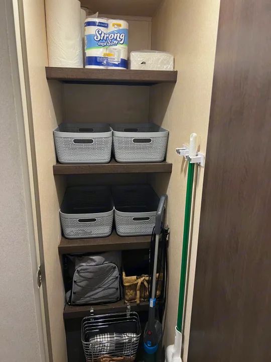 RV rental storage area: shelves filled with toilet paper, cleaning supplies, organizational baskets, a vacuum, and a broom.. Forest River Salem 2019