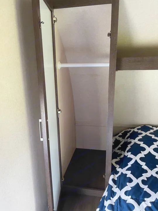 An open RV rental closet with a white hanging rod, dark wood trim, and a bed featuring a blue patterned comforter.. Forest River Salem 2019
