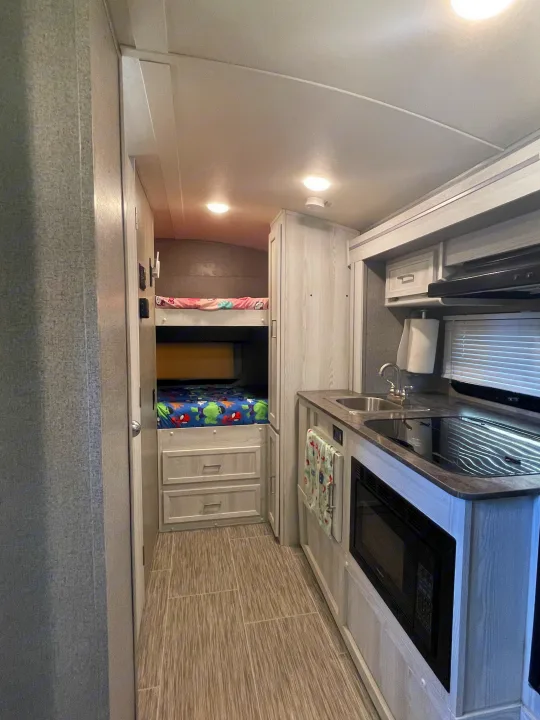 RV rental interior: kitchen with sink/stove, across from bunk beds. Bright and modern with light wood cabinetry.. Forest River Rockwood Geo Pro 2018