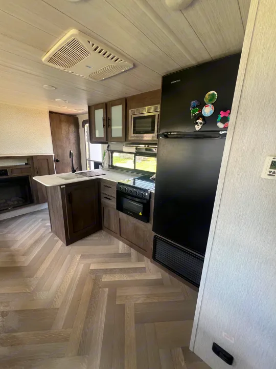 Modern RV rental interior: kitchen with black appliances, light wood herringbone floor, fireplace, and AC unit visible.. Forest River Salem Cruise Lite 2022