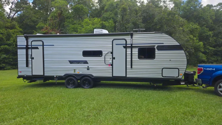 Silver Lake RV rental travel trailer hitched to a blue 4x4 pickup truck, parked on a lush green lawn with trees.. East to West Silver Lake 2024