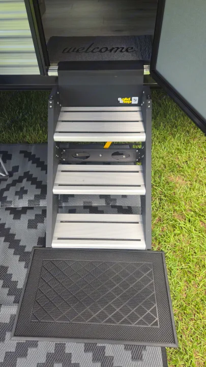Solid Step RV rental entry: indoor 'welcome' mat and outdoor patterned rug on green grass.. East to West Silver Lake 2024