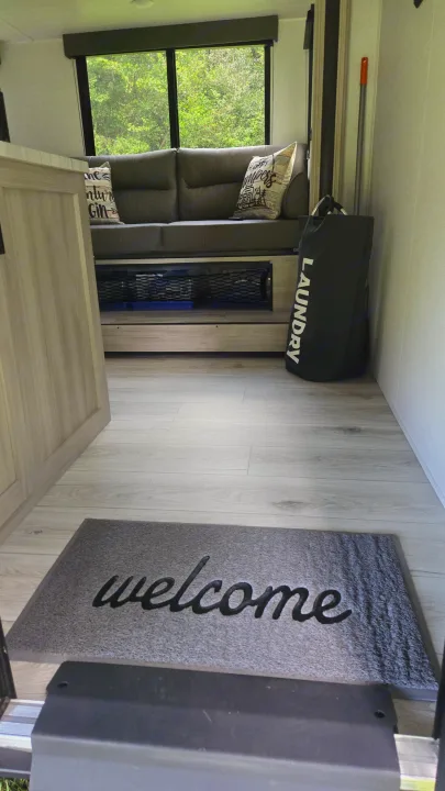 Cozy RV rental interior: "welcome" mat, light flooring, sofa with storage, and a scenic window view.. East to West Silver Lake 2024