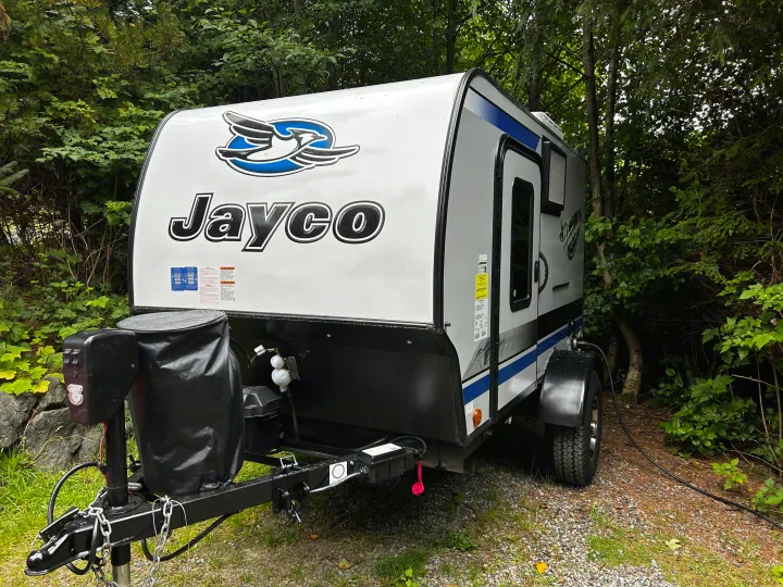 Small white Jayco travel trailer, ideal for an RV rental adventure. Parked on gravel among lush green trees.. Jayco Hummingbird 2019