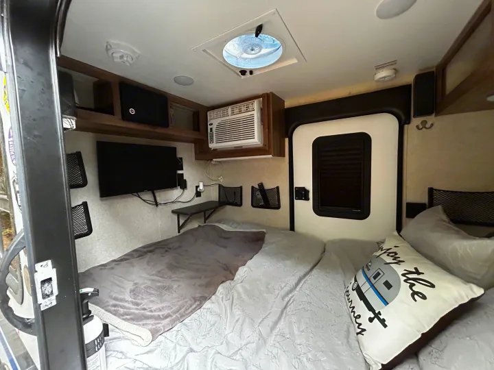 Cozy RV rental bedroom with bed, wall-mounted TV, AC, and storage. Perfect for compact travel.. Jayco Hummingbird 2019