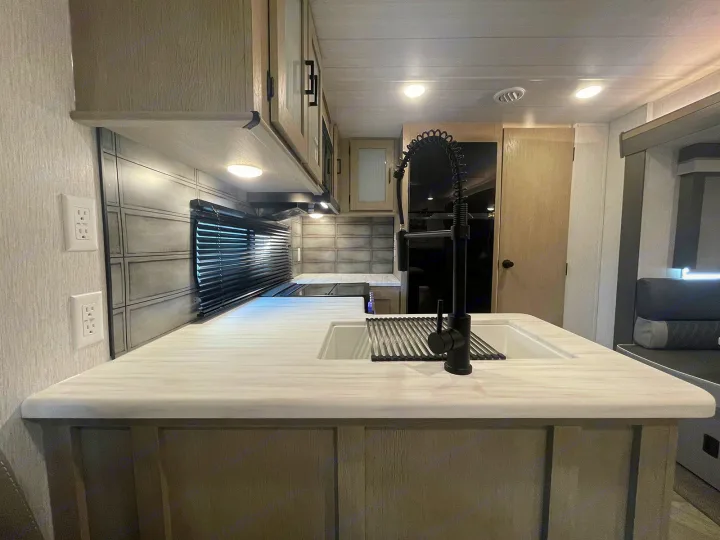 RV rental kitchen: stylish interior with white countertops, sink, black faucet, light wood cabinets, and cozy seating.. Forest River Wildwood 2022