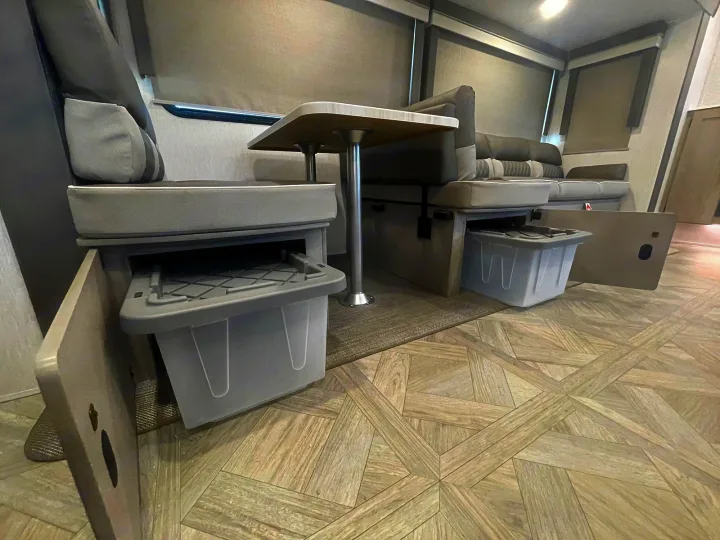 Inside this **rv rental**: a modern dining booth with comfy seating, a table, and smart pull-out storage bins.. Forest River Wildwood 2022