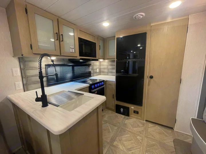 Modern RV rental kitchen: light wood cabinets, black appliances, light countertops, and stylish tile backsplash.. Forest River Wildwood 2022