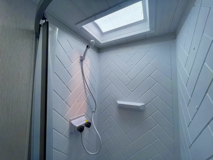 RV rental shower: compact white interior, herringbone walls, showerhead, controls, skylight for bright travels.. Forest River Wildwood 2022