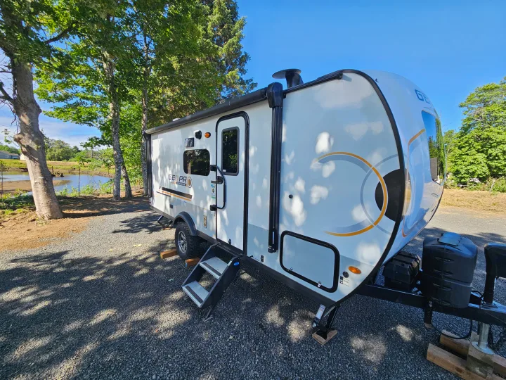 Discover outdoor adventures! This white Geo Pro travel trailer RV rental is set up by water and trees.. Forest River GeoPro 20BHS 2022