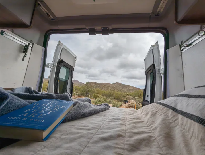 Relaxing in an RV rental, looking out at a stunning desert landscape. A comfy bed, book & blanket await.. Winnebago Solis 2021