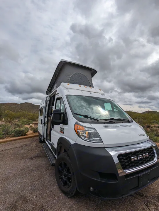 Explore the desert in this white Winnebago pop-top rv rental van, ready for your next adventure with its side door open.. Winnebago Solis 2021