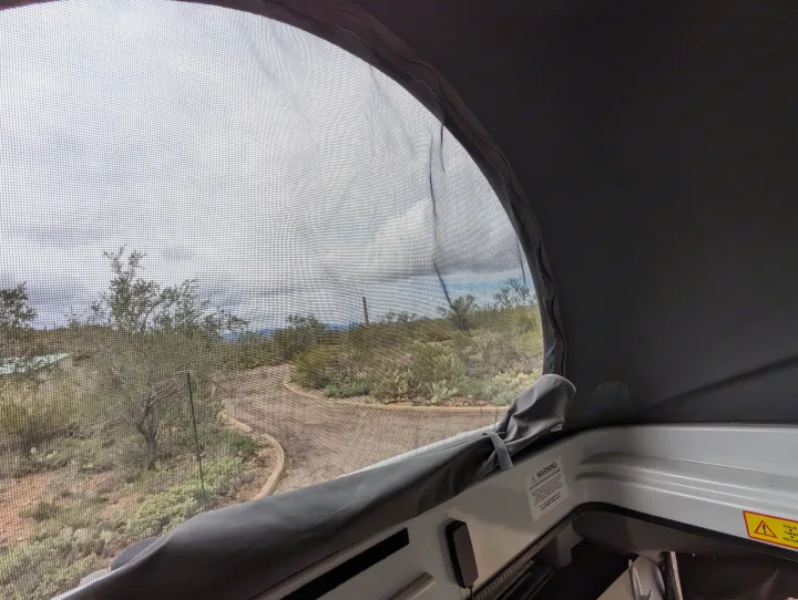 View from an RV rental's screen window overlooking a desert landscape with cacti and a winding road, inside shows a warning label.. Winnebago Solis 2021