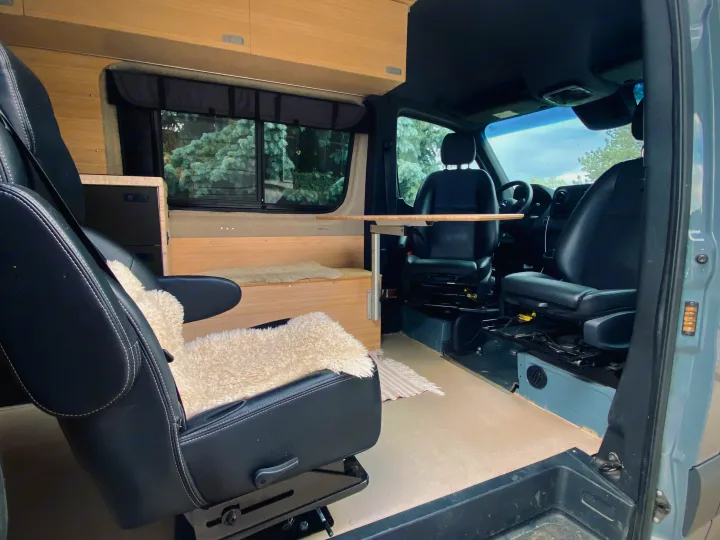 This rv rental camper van's interior showcases swiveling front seats, a wooden table, and built-in cabinetry.. Mercedes Sprinter 2500 2020
