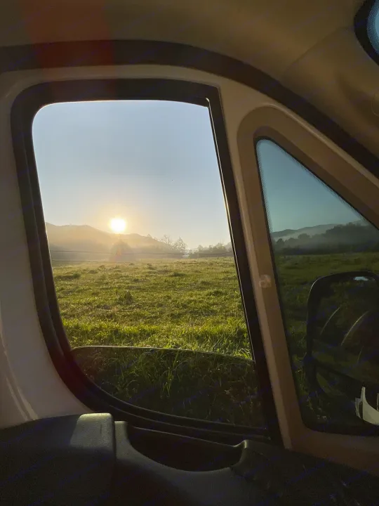 Golden sunrise from our cozy RV rental. Misty fields and mountains welcome a new day on the road.. Thor Sequence 2023