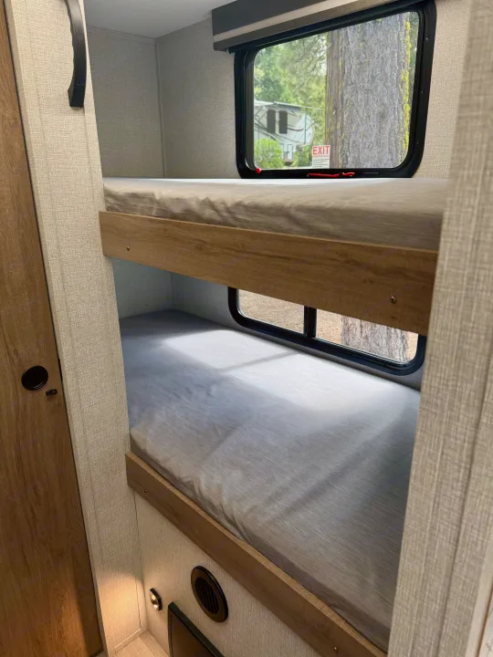 Cozy bunk beds in an RV rental, offering comfortable sleeping quarters with views of nature outside the window.. Grand Design Imagine AIM 2024