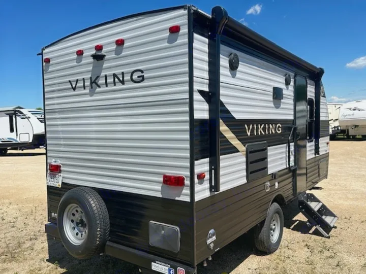 This grey and black Viking travel trailer is an ideal RV rental option, seen from the rear with a spare tire and side steps.. Viking SAGA 17FQS 2022
