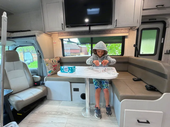 A child plays dominoes inside a modern rv rental, enjoying family fun at the dinette table.. Forest River Coachmen Freelander 2025