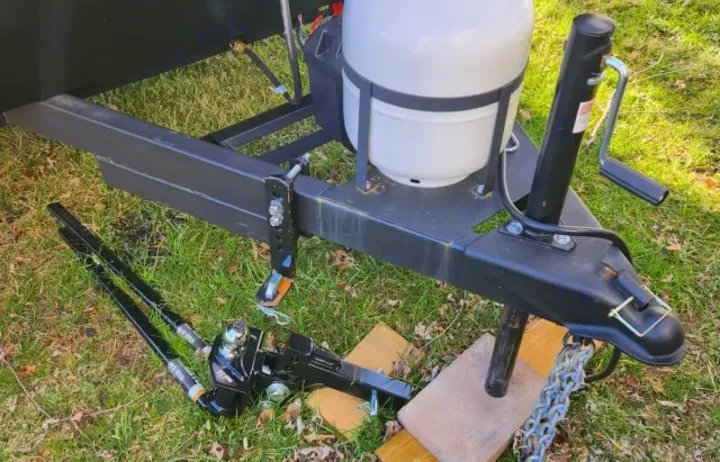 RV rental trailer's front, showing hitch, propane tank, jack, and weight distribution system on ground, crucial for safe towing.. Keystone RV Hideout Sport 2024