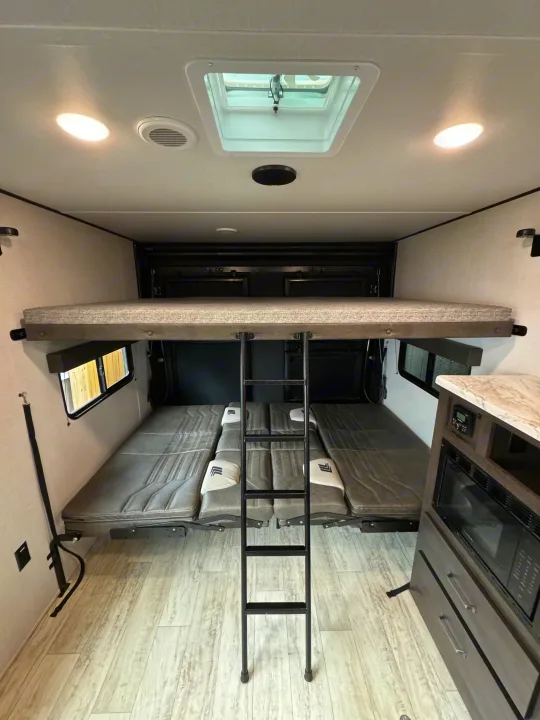 Inside an RV rental: a top bunk, convertible lower beds with a ladder, and a kitchen area, all with bright lighting.. Grand Design Grand Design Trailer 2024