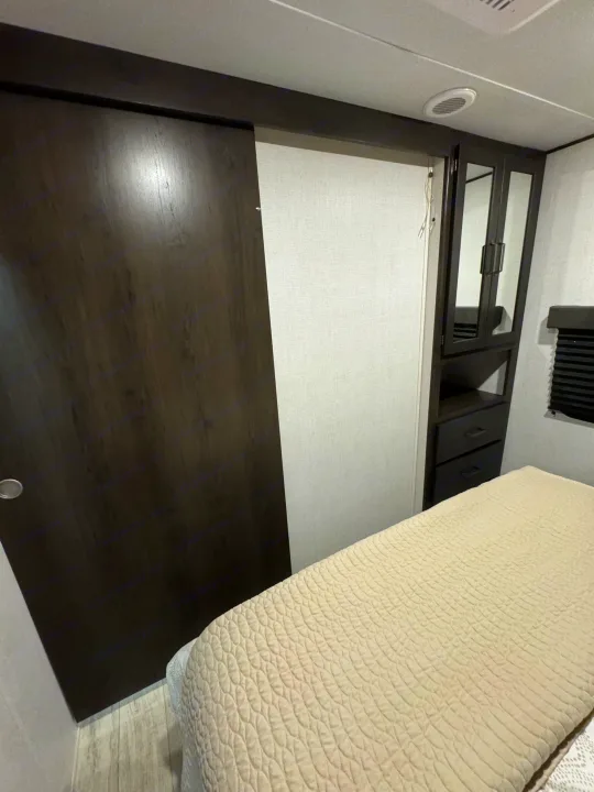 RV rental bedroom: dark sliding door, mirrored closet, drawers, and light quilted bed for compact comfort.. Grand Design Grand Design Trailer 2024