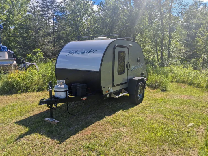 Bushwhacker teardrop camper, an ideal RV rental for your outdoor adventures. Parked in a sunny, grassy area with trees.. Braxton Creek Bushwhacker 2021