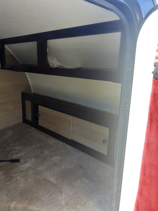 RV rental interior showing compact storage with open shelves, wood-look cabinets, and a textured floor.. Braxton Creek Bushwhacker 2021