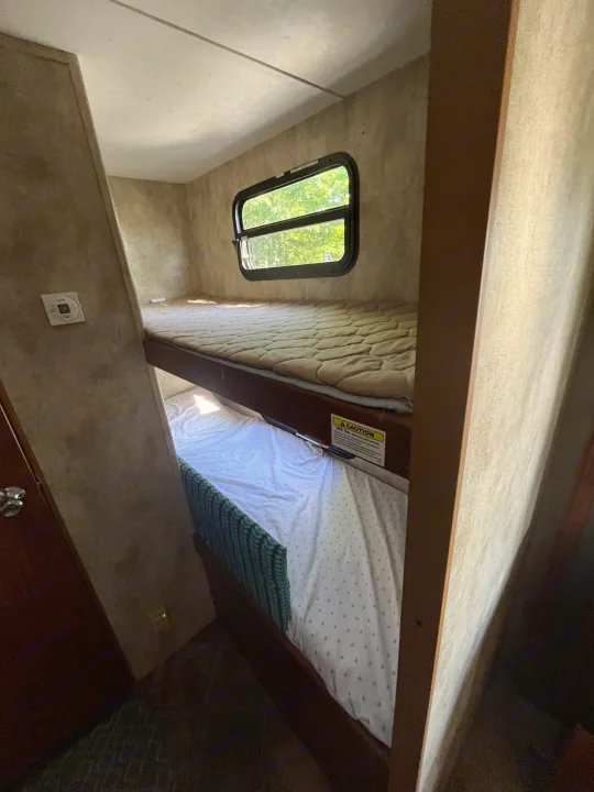 Inside an RV rental: Compact sleeping area with upper and lower bunk beds, window, and wall controls.. Keystone RV Passport Ultra 2013