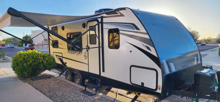 White & black Passport travel trailer RV rental with awning extended, parked outdoors. Perfect for your next adventure.. Keystone RV Passport SL 2022
