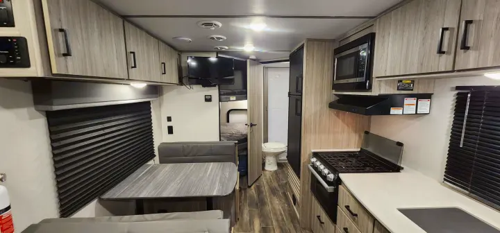 Bright RV rental interior with a fully equipped kitchen (stove, microwave), dinette, TV, bunk beds, and a compact bathroom.. Keystone RV Passport SL 2022