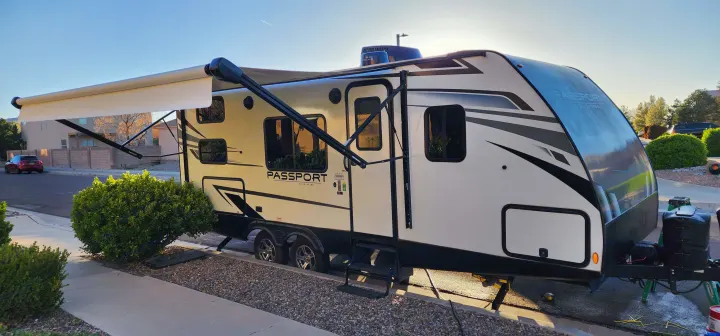 A white and black Keystone Passport travel trailer, ideal for an rv rental, is parked with its awning extended under a bright sky.. Keystone RV Passport SL 2022