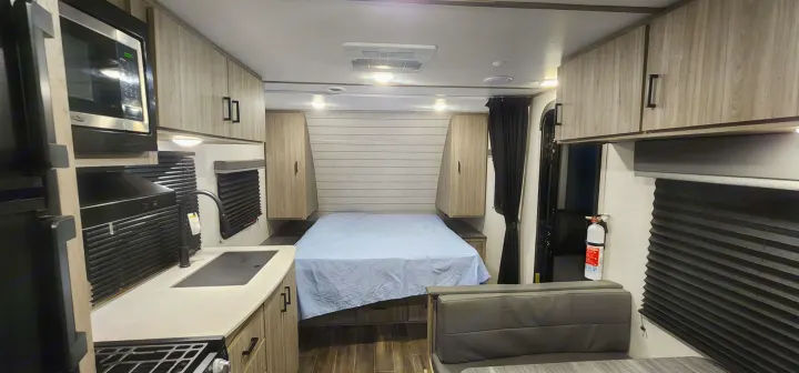 RV rental interior: kitchen with microwave and sink, cozy bedroom with bed, and dinette. Modern, compact living space.. Keystone RV Passport SL 2022