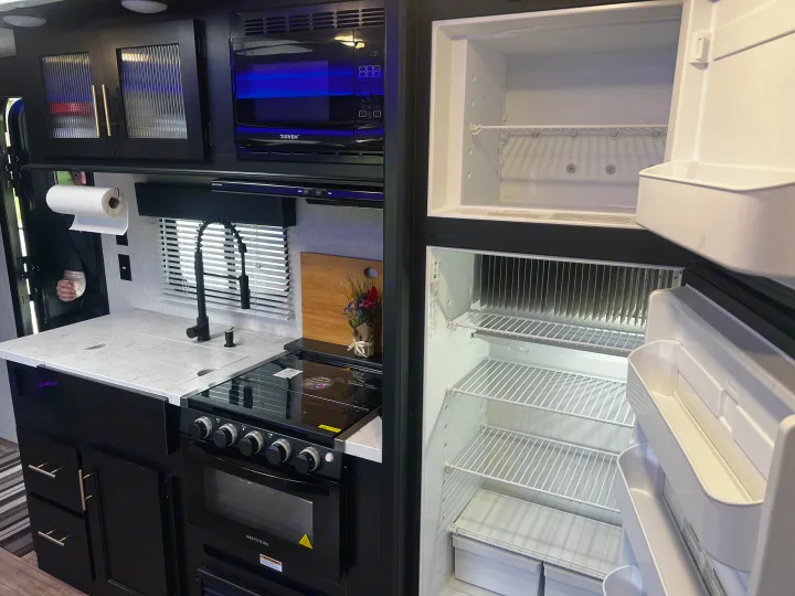 Modern RV rental kitchen: sleek black appliances, including an open fridge, microwave, stove, and stylish cabinets.. Forest River Cherokee Grey Wolf 2021