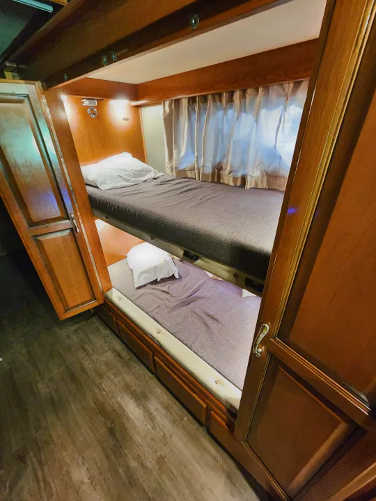 Explore this RV rental's functional interior featuring stacked bunk beds with comfy grey mattresses and wooden cabinets.. Fleetwood Bounder 2018