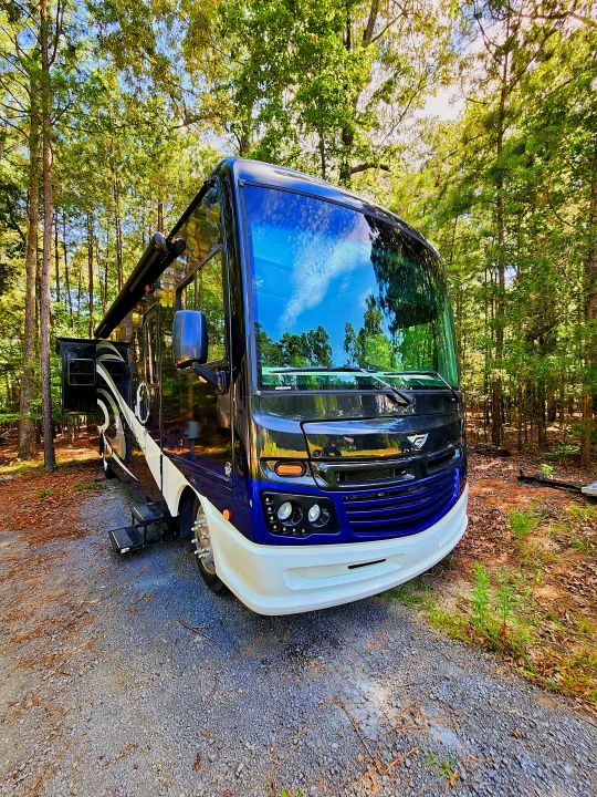Modern RV rental parked on gravel in a lush, green forest campsite, sunlight dappling through trees.. Fleetwood Bounder 2018