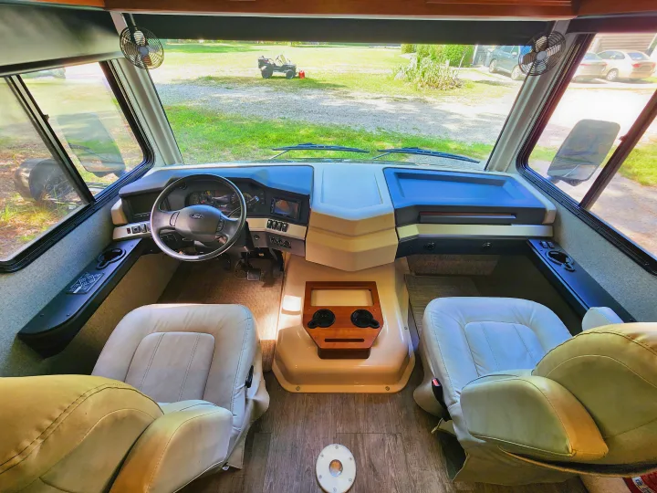 Spacious RV rental cockpit with steering wheel, dashboard, front seats, and a clear view ahead.. Fleetwood Bounder 2018