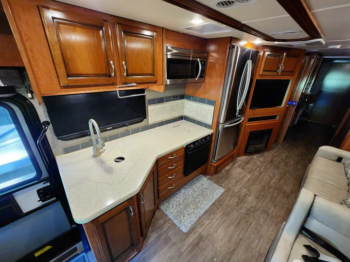RV rental interior: modern kitchen with light counters, full-size fridge, fireplace, and sofa.. Fleetwood Bounder 2018