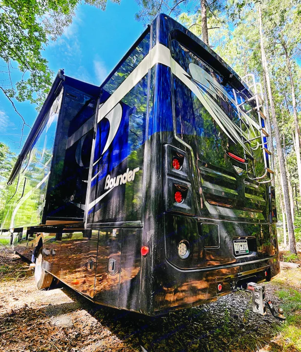Spacious black RV rental, a Fleetwood Bounder motorhome, parked in a sunny forest setting with slide-out extended.. Fleetwood Bounder 2018