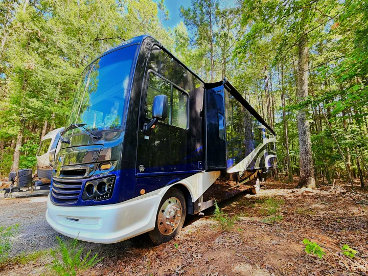 This dark blue and white rv rental motorhome is parked in a sunny, tree-filled campsite, perfect for outdoor adventures.. Fleetwood Bounder 2018