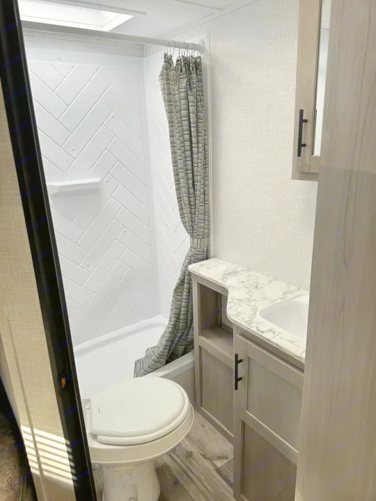 Compact RV rental bathroom features a modern shower, toilet, and vanity with marble-look counter.. Dutchmen Coleman Light 2022