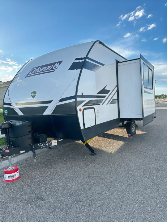 A white Coleman RV, ideal for an RV rental, is parked on asphalt with its side slide-out extended under a blue sky.. Dutchmen Coleman Light 2022