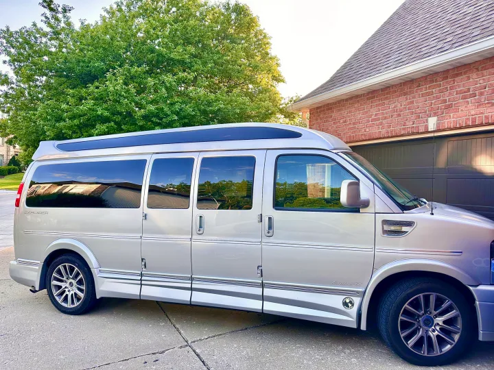 Silver Explorer conversion van, ideal for RV rental, parked on a driveway next to a brick house and tree.. CHEVROLET Cargo Van 2020