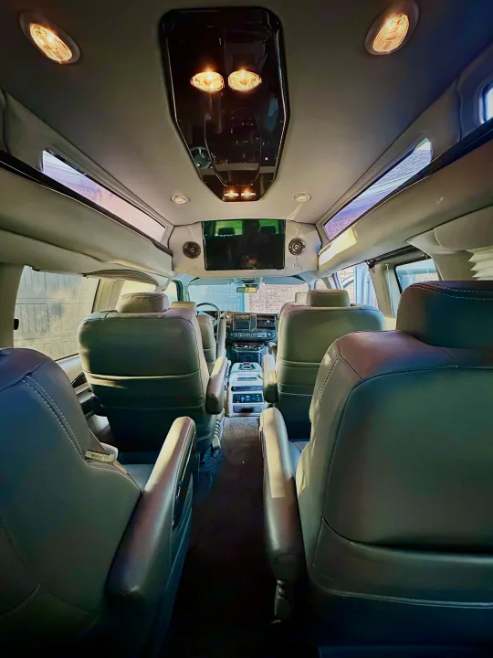 Spacious RV rental interior featuring black leather captain's chairs, overhead lighting, and a ceiling-mounted TV for comfort.. CHEVROLET Cargo Van 2020
