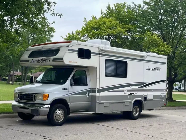 This white and gray Fleetwood Jamboree Class C RV rental, a spacious recreational vehicle, is parked roadside.. Jamboree Jamboree Motorhome 2004