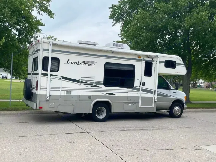This white & gray Jamboree RV rental, with its awning out, is parked on a street, ready for your next trip.. Jamboree Jamboree Motorhome 2004