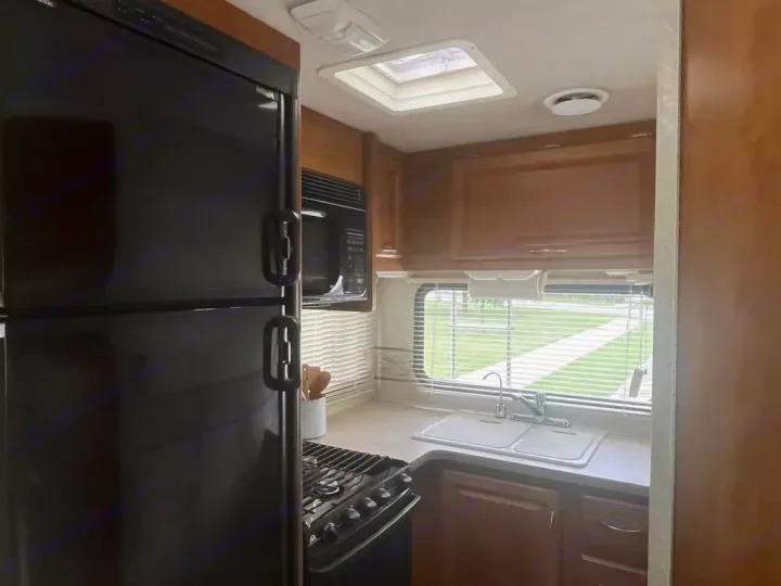 Spacious RV rental kitchen featuring a large black refrigerator, microwave, stove, and double sink with a window view.. Jamboree Jamboree Motorhome 2004