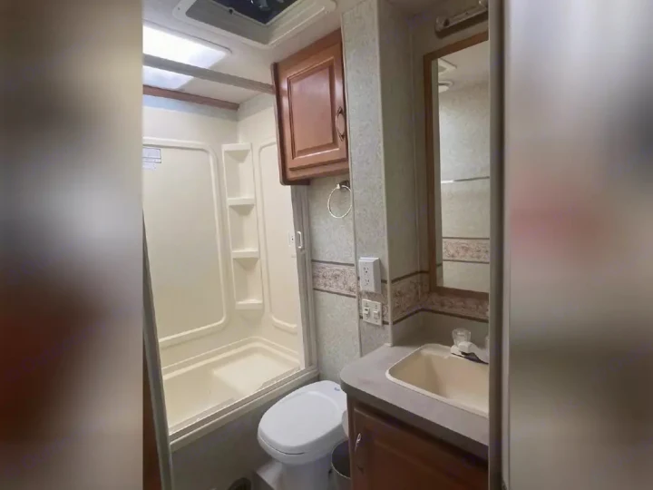 Compact RV rental bathroom features a shower, toilet, and vanity with sink & mirror, designed for efficient use of space.. Jamboree Jamboree Motorhome 2004