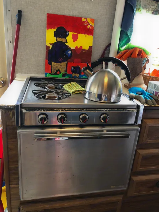 Cooking setup in an RV rental: a compact stainless steel stove with a kettle and a colorful painting on the wall.. Vintage Trailers Skylark 180 1979