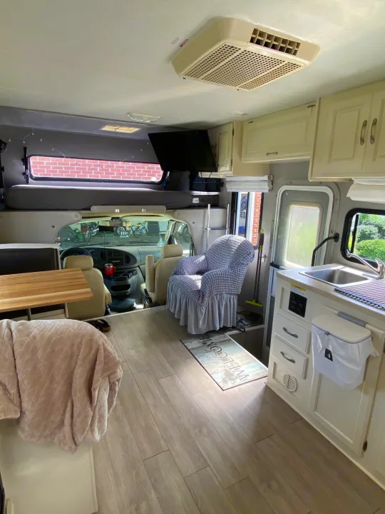 Cozy RV rental interior: kitchen, armchair, overhead bed, and driver's area visible. Light wood floors throughout.. Four Winds 5000 2008